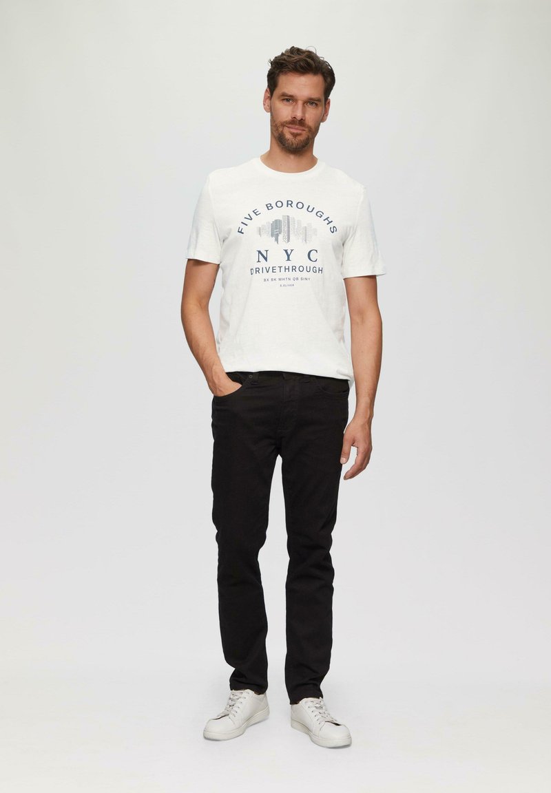 Witte t-shirt met korte mouwen en marineblauwe tekst "FIVE BOROUGHS NYC DRIVETHROUGH," gecombineerd met zwarte jeans en witte sneakers. Eenvoudig ontwerp, casual pasvorm.