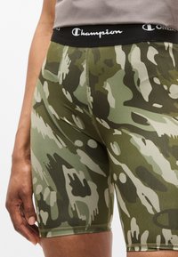Πράσινα καμουφλάζ σορτς από ελαστικό ύφασμα, με μαύρη μέση που φέρει το λογότυπο "Champion" και απαλή υφή.