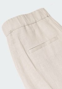 Pantalon en lin beige avec une taille élastique. Il présente une poche arrière unique à design dissimulé et une finition lisse et texturée.