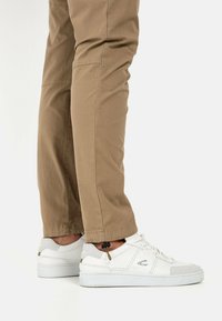 Weiße Sneaker mit grauen Akzenten und strukturierten Details, kombiniert mit khakifarbenen Hosen mit Seitentaschen und einer schmal zulaufenden Beinform.