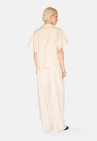 Beige Hemd mit kurzen Ärmeln und lässiger Passform sowie Rückenschlitz, kombiniert mit weit geschnittenen Hosen aus einem ähnlichen Stoff, die einen stimmigen Look kreieren.