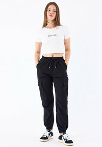 Hvid cropped t-shirt med sort tekst, parret med sorte cargo joggers med elastisk talje og lommer, samt sort og hvid sneakers.