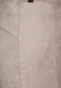 Beige suède stof met een zachte, gladde textuur en zichtbare stiksels. Bevat hoekige naaddetails voor een gestructureerd ontwerp.