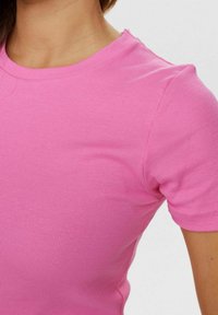 Różowy, prążkowany t-shirt z krótkim rękawem i okrągłym dekoltem. Materiał wydaje się miękki, z delikatną teksturą i dopasowanym krojem.