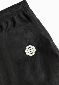 Zwarte shorts met een gestructureerde afwerking, voorzien van een elastische tailleband en een wit logopatch op de achterzak.