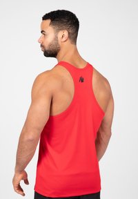 Rode sportieve tanktop met een racerback ontwerp. Gemaakt van een soepel materiaal, met een klein zwart logo op de bovenrug.