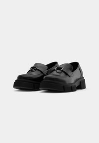 Black leather shoes with a chunky sole, featuring a wide strap and metal ring accent. Smooth texture with a rounded toe design.