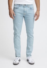 Ljust blå denimjeans med slim fit, femficksdesign och subtila sömnadsdetaljer, i kombination med vita träningsträn.