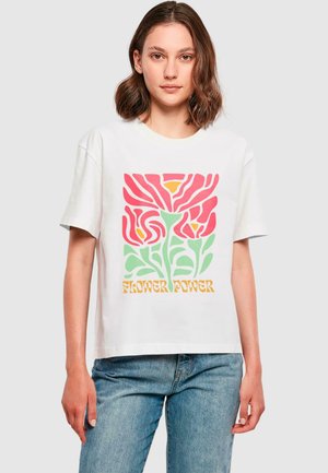 T-shirt en coton blanc avec un graphisme de fleurs stylisées en rouge, orange et vert, et le texte "Flower Power" en jaune en bas.