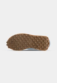 Suela de zapato deportivo con goma texturizada marrón, con studs rectangulares y circulares para mejor agarre. Parte superior y detalles en el borde de color azul claro.