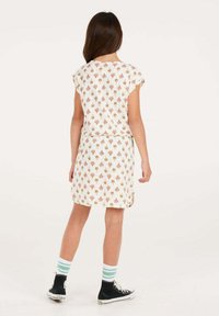 Witte jurk met korte mouwen, met een herhaald bloempatroon in oranje en roze. Gecombineerd met zwarte hoge sneakers en gestreepte sokken.