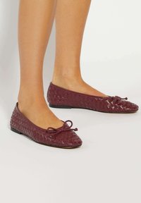 Burgundy woven leather ballet flats with a pointed toe and bow detail, featuring a flat sole and textured finish for grip.
