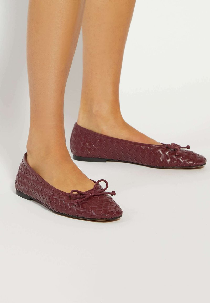 Burgundy woven leather ballet flats with a pointed toe and bow detail, featuring a flat sole and textured finish for grip.