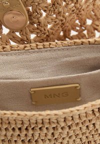 Braided straw bag with tan fabric lining. Features a gold-tone snap closure and an interior label with "MNG" embossed. Textured surface throughout.