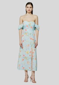 Abito a fiori in tessuto azzurro chiaro, con maniche scoperte sulle spalle, uno spacco alto fino alla coscia e un corpetto aderente. Tacchi trasparenti completano il look.