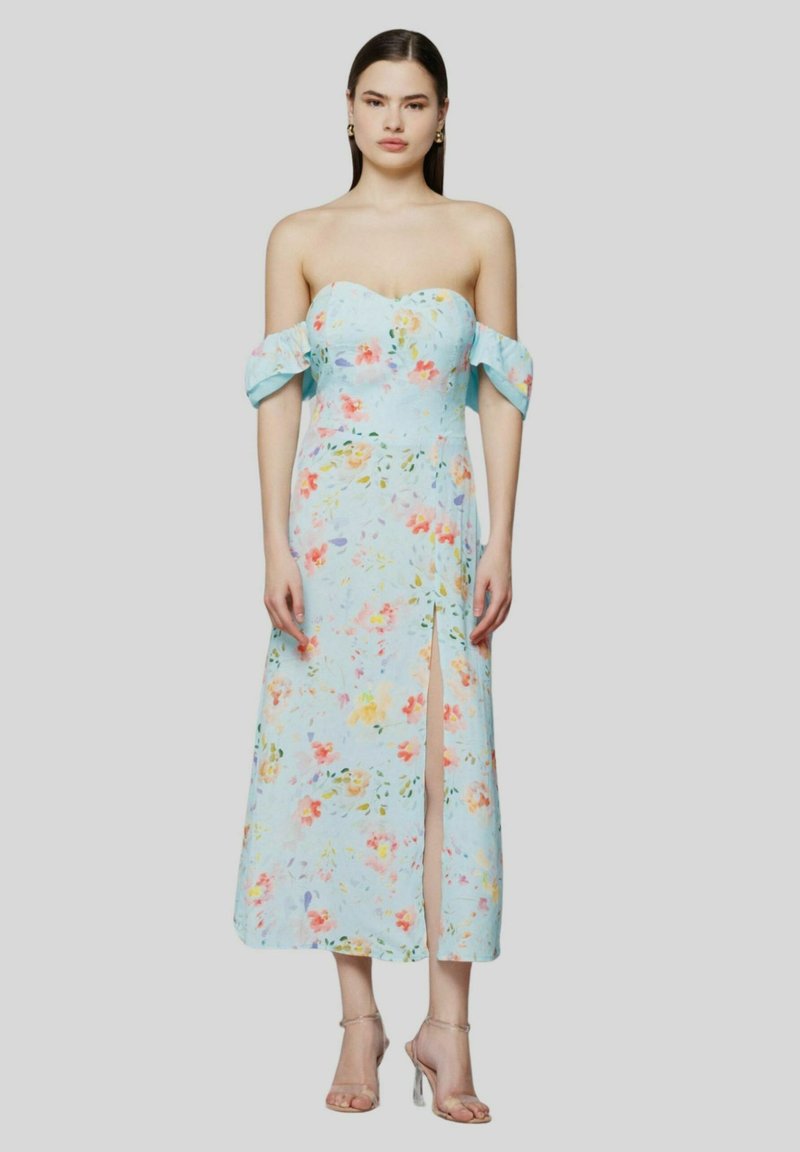 Abito a fiori in tessuto azzurro chiaro, con maniche scoperte sulle spalle, uno spacco alto fino alla coscia e un corpetto aderente. Tacchi trasparenti completano il look.