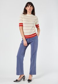 Knit short-sleeve top with ivory, red-striped pattern; paired with light blue trousers and shiny black heels featuring decorative accents.