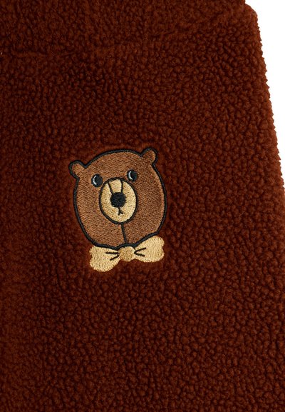 Tecido de lã castanho com o rosto de um urso bordado e uma gravata-borboleta, apresentando orelhas arredondadas, olhos pretos e um focinho bege.