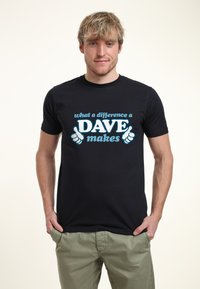 Camiseta de algodón negra con texto azul que dice "qué diferencia hace un DAVE", con dos gráficos de pulgares arriba en el frente. Mangas cortas, cuello redondo.