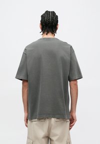 Szürke pamutpóló rövid ujjakkal, laza szabású, kerek nyakkivágással. Az alsó szegély hátul enyhén hosszabb. Egyszerű, logó nélküli dizájn.