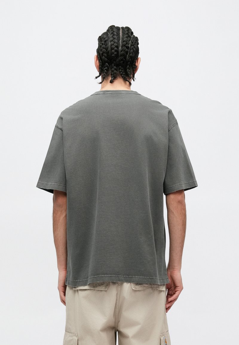 Grå bomullst-shirt med korta ärmar, ledig passform och rund halsringning. Nederkanten är något längre baktill. Enkel design utan synliga logotyper.