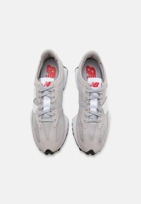 Chaussures de sport grises en mesh et en daim, avec une bande blanche, des lacets gris et des accents rouges sur les semelles intérieures.