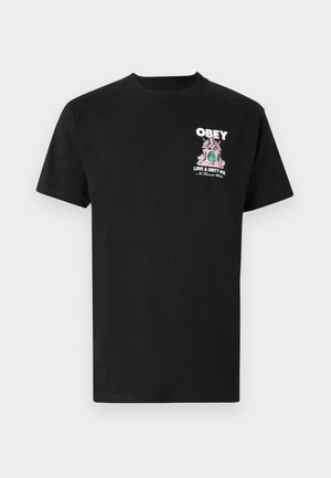 T-shirt em algodão preto com um estampado gráfico em rosa e verde que inclui o texto "OBEDEÇA" e "AMOR E UNIDADE JÁ" na frente.