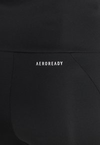 Gros plan sur un tissu noir avec le logo blanc «AEROREADY» imprimé sur une couture, mettant en valeur un matériau de vêtements de sport qui évacue l'humidité.