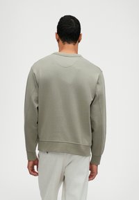 Světle olivově zelená mikina se volným střihem, žebrovanými manžetami a lemem. Hladká textura se jemným švem na zadní straně.