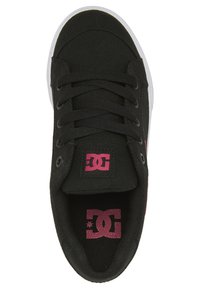 Schwarzer Leinenschuh mit runder Zehenpartie, flachen Schnürsenkeln und lila DC-Logo auf der Zunge. Weiße Gummisohle und schwarze Innenausstattung.