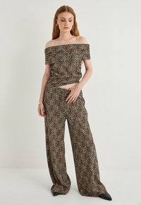 Leopardenmuster Top mit schulterfreiem Schnitt, kombiniert mit weit geschnittenen Hosen. Der Stoff ist glatt und hat eine sanfte Textur; die Farben umfassen Braun, Schwarz und Beige.