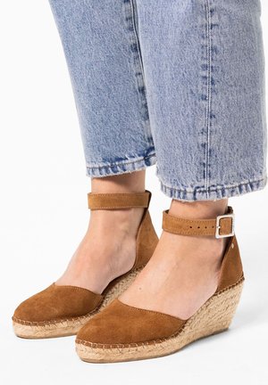 Braune Wildleder-Wedge-Sandaletten mit Knöchelriemen, gewebter Jutesohle und abgerundeter Zehe, kombiniert mit hellen, gewaschenen, kurz geschnittenen Jeans.