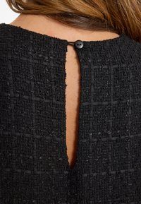 Schwarzer, strukturierter Stoff mit einem gewebten Muster; verfügt über eine Rückenschlitzöffnung, die mit einem einzelnen Knopf gesichert ist.