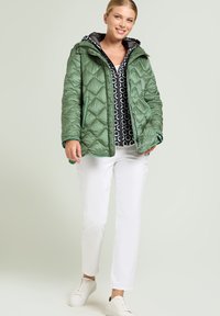 Padded green quiltowana kurtka z kapturem, z czarną podszewką i w geometryczne wzory na górze. Połączona z białymi spodniami i tenisówkami.