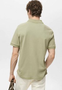Kurzarm-Polo aus leicht grünem Stoff, mit klassischem Kragen und lockerer Passform, schimmernder Textur und subtilen Nähten.