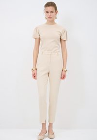 Beige short-sleeve top with puff sleeves, paired with beige tailored trousers featuring a slim fit and side slits. Simple design and texture.