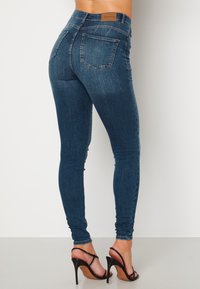 Úzké modré denimové džíny s vysokým pasem, designem s pěti kapsami, kontrastním prošíváním a štítkem na zadní straně.