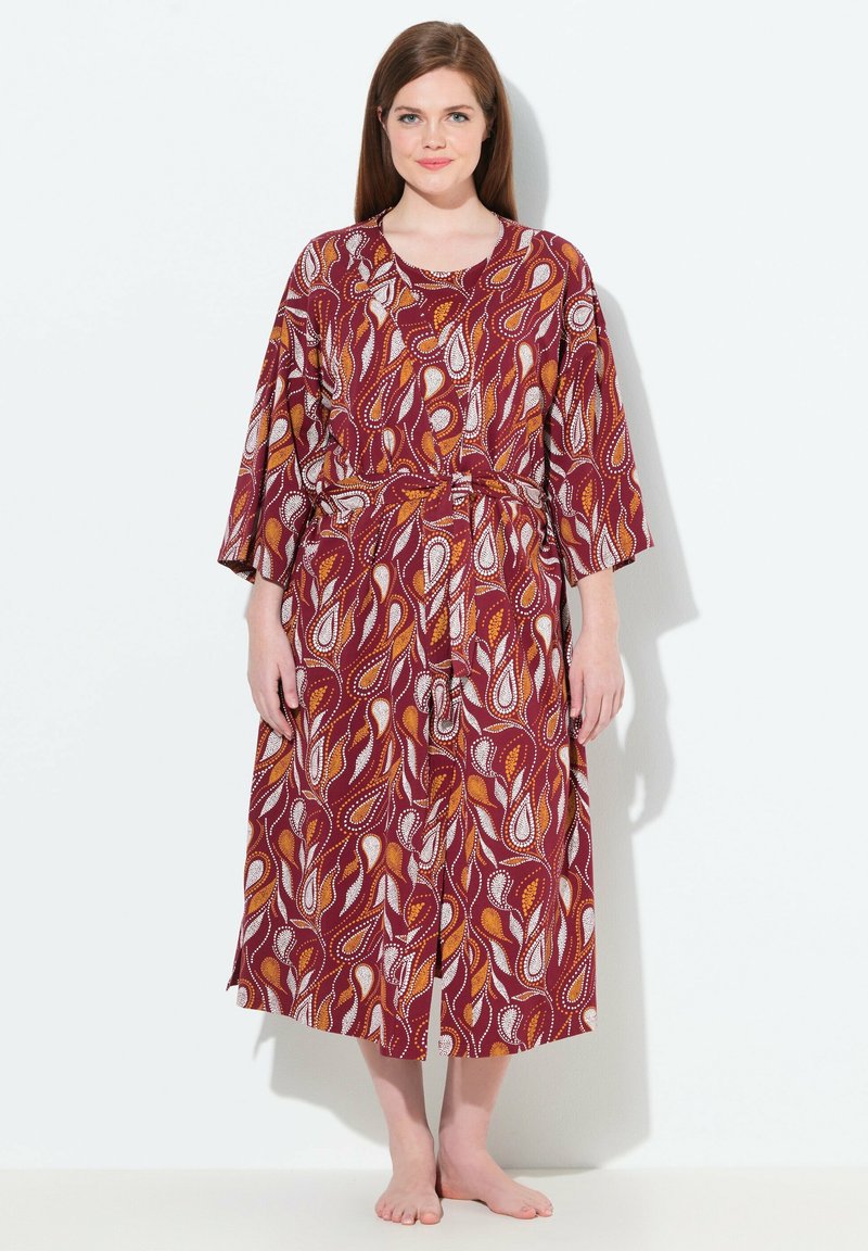 Dlouhé šaty s červeným a bílým vzorem, širokými rukávy, úzkým pasem a splývavým siluetou. Materiál má hladkou texturu, ideální pro pohodlí.