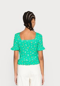 Top floral verde com mangas curtas e onduladas, textura franzida e decote quadrado. Apresenta uma barra em peplum e pequenos padrões de flores multicoloridas.