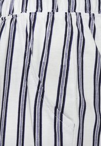 Die Baumwollshorts sind aus einem weißen Stoff mit dunkelblauen vertikalen Streifen gefertigt. Sie haben einen elastischen Bund und seitliche Taschen. Die Textur wirkt weich und atmungsaktiv.