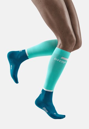 Calzini alti fino al ginocchio in teal sfumato con materiale testurizzato; presentano una punta e un tallone blu scuro solidi, con accenti di logo bianchi.