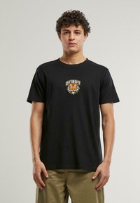 Tricou din bumbac negru cu un grafic frontal reprezentând un tigru și textul "DETROIT" scris cu litere albe cu margine colorată. Mâneci scurte și gât rotund.