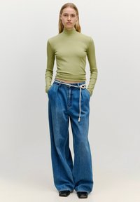 Olivgrünes, geripptes Langarmoberteil, kombiniert mit lockeren blauen Jeans mit Kordelzugbund. Glatte Textur und lässige Passform.