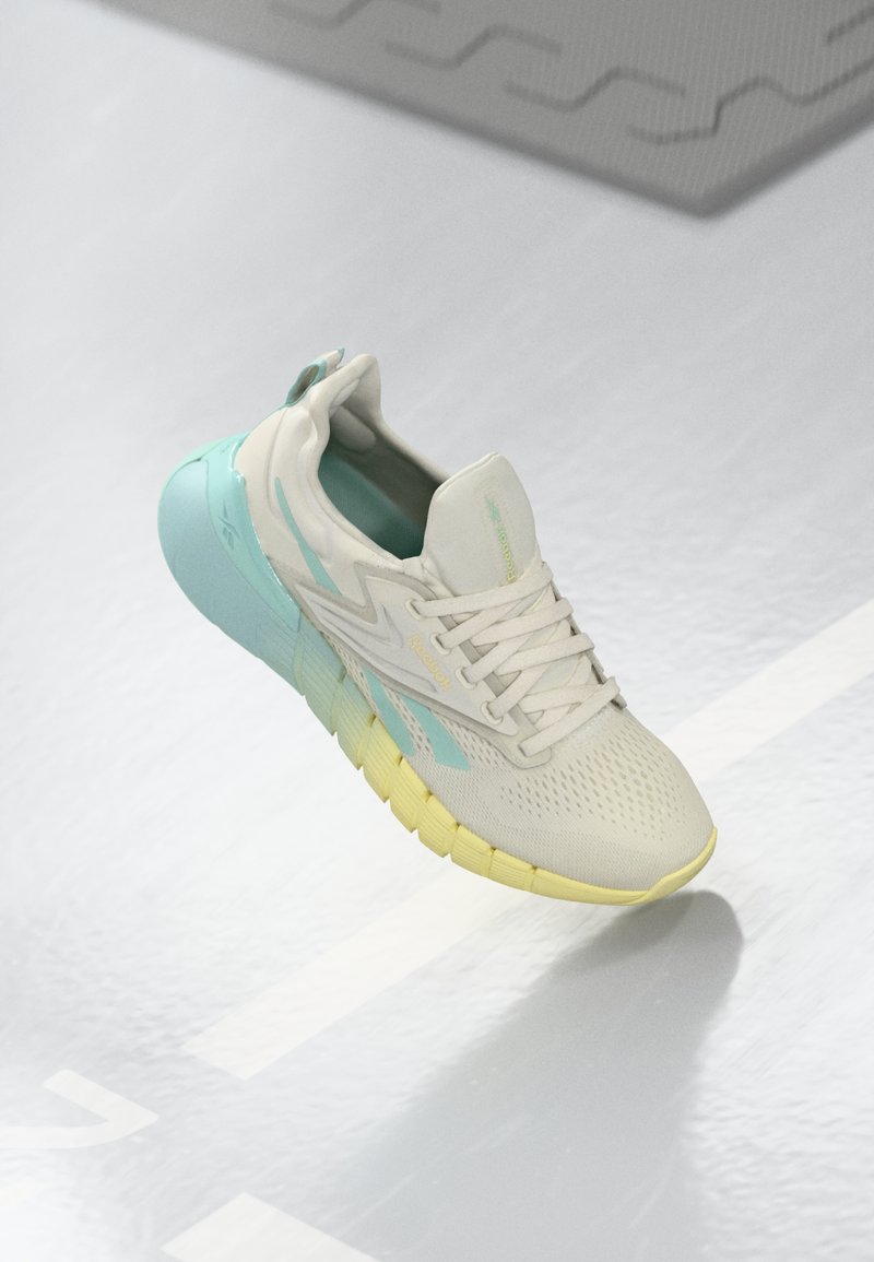Zapatilla de correr ligera con una parte superior de malla beige, acentos en azul aqua y una suela texturizada amarilla. Cuenta con una plantilla acolchada y cordones.
