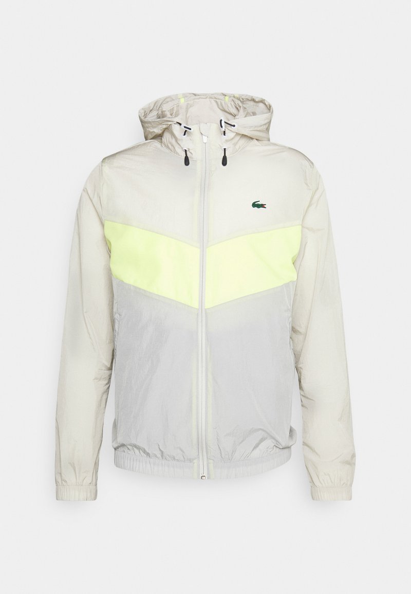 Licht beige en lichtgrijze hooded jacket met neongele chevronstreep en groen krokodillenlogo op de borst, met rits aan de voorkant.