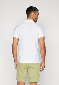 Weißes Poloshirt mit kurzen Ärmeln, glatter Stoff, mit geripptem Kragen. Getragen mit hellgrünen Shorts mit Seitentaschen und weißen Akzenten.