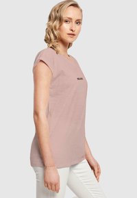 Šviesiai rožinė trumpa rankovė t-shirt, pagaminta iš minkštos medžiagos, su juodu užrašu "BELIEVE" priekyje ir laisva apykakle.