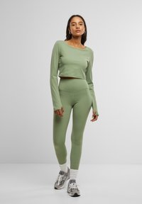 Világoszöld sportos szett, amely egy rövidujjú, hosszú ujjú toppból és magas derekú leggingsből áll, mindkettő sima textúrájú, szürke sportcipővel párosítva.