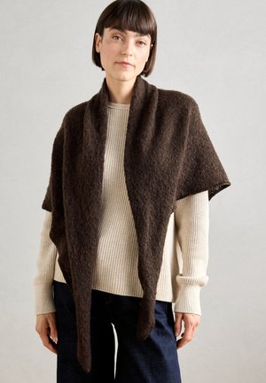 Brown knitted shawl with an open front, made of soft textured fabric, draping around the shoulders, paired with a cream-colored sweater.