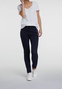 Vit V-ringad t-shirt i kombination med marinblå joggingsbyxor med sidofickor och dragsko, kompletterat med vita sneakers.